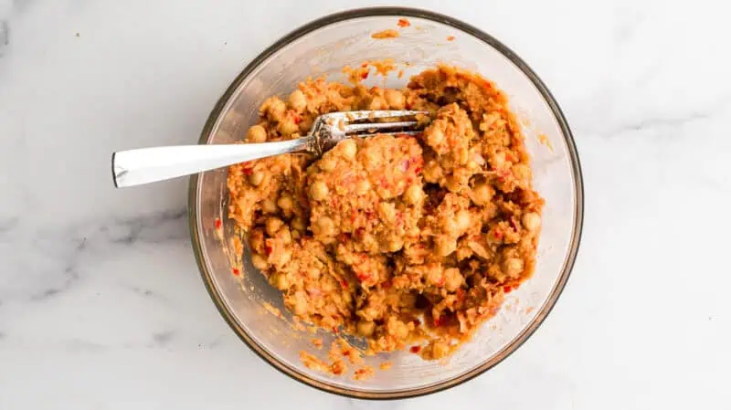 Chickpeas mashed into fritter mixture in glass bowl.