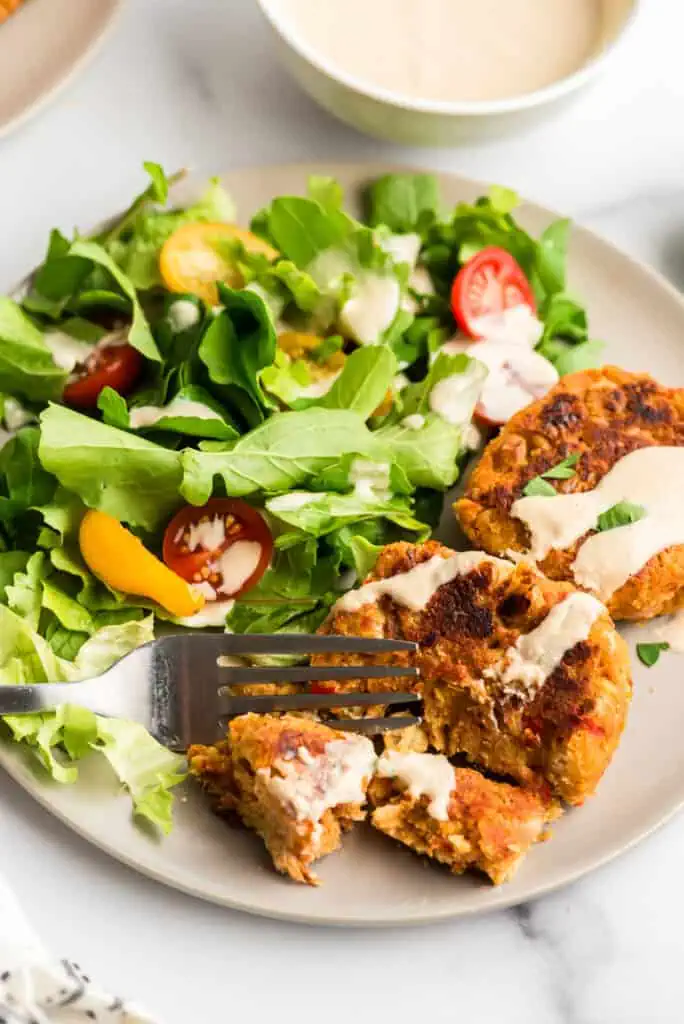 Fork cutting into chickpea fritter on plate with salad.