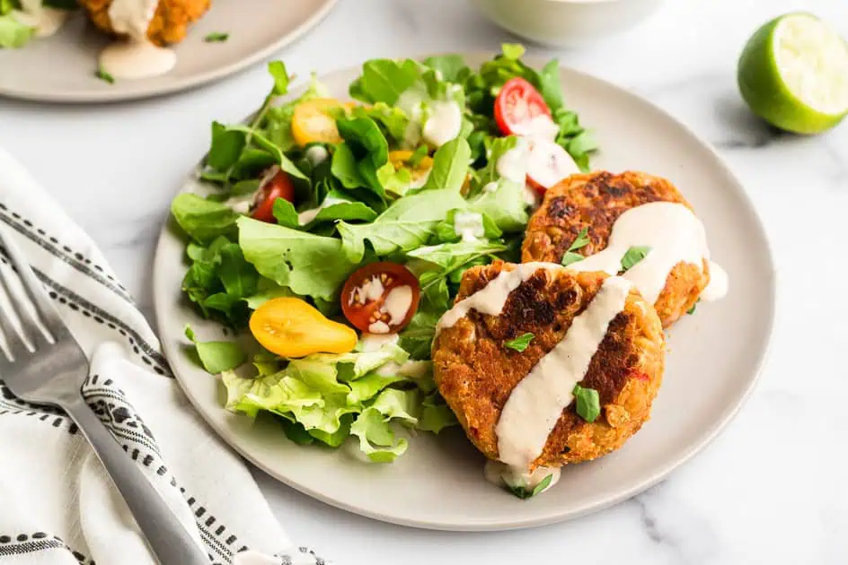 Two chickpea fritters on white plate with salad in background. 