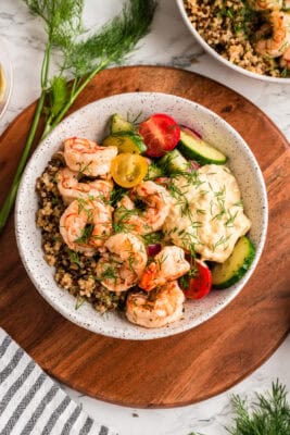 Greek shrimp and quinoa bowl with hummus on a wooden plate.