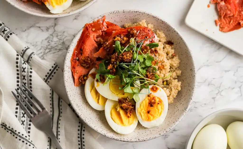 Bowl filled with quinoa, smoked salmon, hard boiled eggs topped with microgreens. 